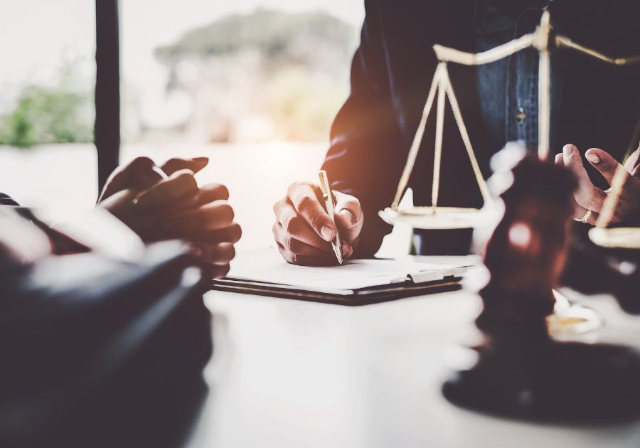 Lawyer Holding Out a Pen to Fill Out a Legal Form Next to the Scales of Justice