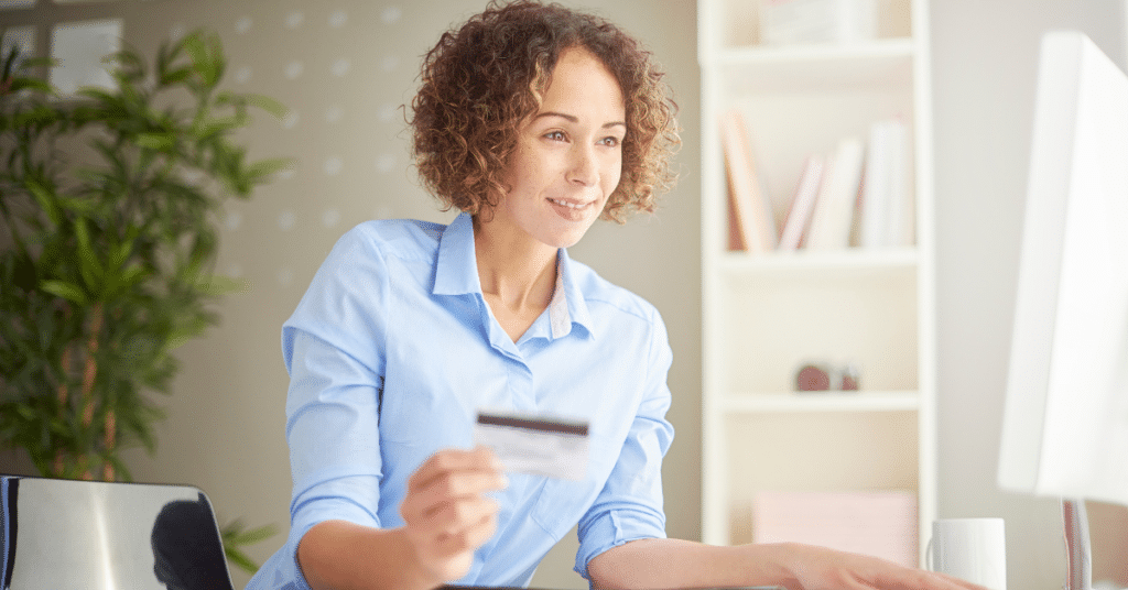 Person holding credit card and looking at desktop computer